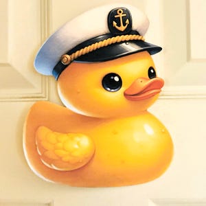 Könnte beinhalten: Eine fröhliche gelbe Quietscheente mit einer weiß-blauen Kapitänsmütze mit goldener Kordel und Ankeremblem. Die Ente hat große schwarze Augen und einen orangefarbenen Schnabel, was ein maritimes Thema hervorruft.