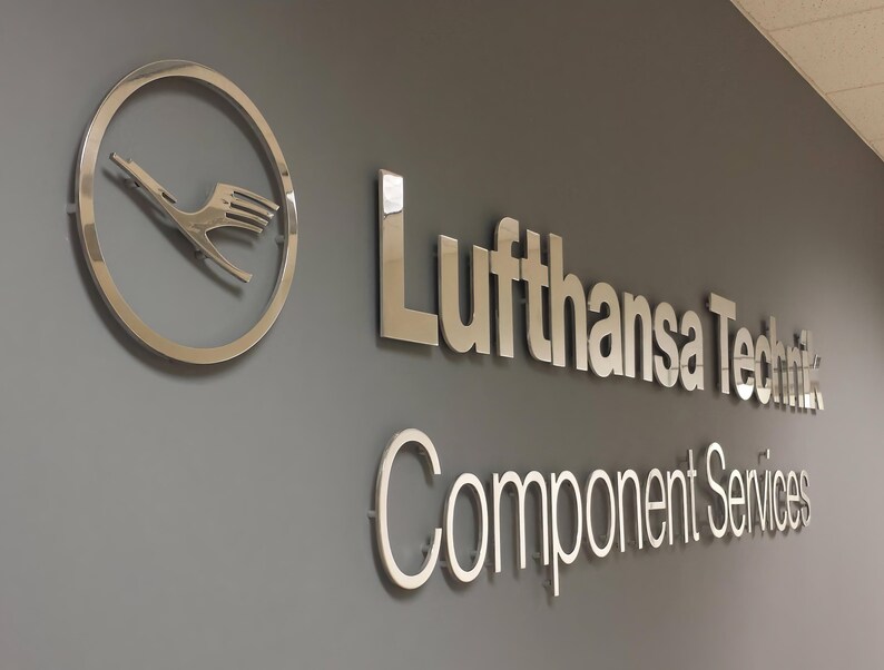 3D logo wall sign made with polished or brushed metal for a custom lobby sign in stainless metal on a dark wall in a modern conference room
