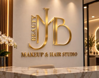Könnte beinhalten: Ein Wandschild mit den goldfarbenen Buchstaben NJB und dem vertikal ausgerichteten Wort BEAUTY, wobei der Text MAKEUP & HAIR STUDIO darunter angebracht ist. Die Beschilderung befindet sich an einer hellen Wand über einem Marmortresen.