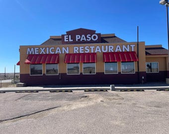 Pode incluir: Vista exterior do restaurante mexicano El Paso. O edifício tem uma fachada bege e bordô com toldos vermelhos sobre as janelas. O nome do restaurante é exibido em letras brancas grandes. O céu está limpo e azul.