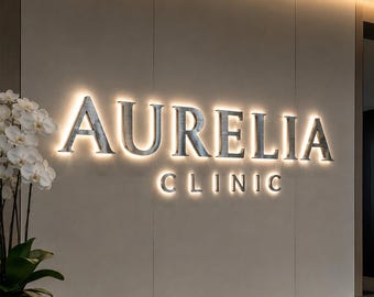 Pode incluir: Letras metálicas retroiluminadas que soletraram "AURELIA CLINIC" numa parede neutra. As letras brilham, criando um efeito marcante. O texto "Custom Backlit Metal Letters" também é visível.