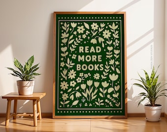 May include: A framed art print with a dark green background and a floral design in cream. The text "READ MORE BOOKS" is centered. The print is displayed on a wooden floor, next to a small wooden table with a potted plant.