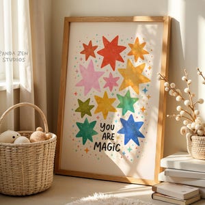 May include: A framed art print featuring colorful star illustrations in red, pink, yellow, green, and blue. The words "You Are Magic" are written below the stars. A woven basket with stuffed toys and decorative branches are in the foreground.