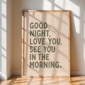 May include: A rectangular wall art print in a light wooden frame featuring a beige background with dark olive green text that reads: GOOD NIGHT, LOVE YOU, SEE YOU IN THE MORNING. A small dark olive green heart symbol follows the final word.