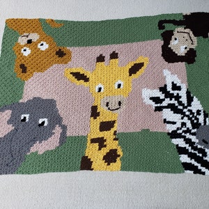 May include: A crocheted blanket featuring a giraffe, zebra, elephant, and lion. The animals are surrounded by a green border and a pink background.