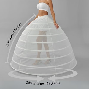 May include: A white bridal petticoat with a hoop skirt design. The petticoat measures 51 inches (130 cm) in height and 189 inches (480 cm) in diameter. The model is wearing a white strapless top and skirt.