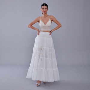 May include: A white layered tulle skirt with a white lace crop top. The model is wearing silver heels.