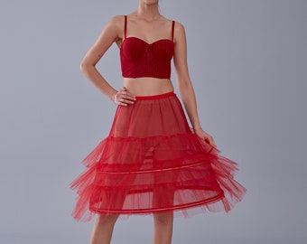 May include: A red tulle petticoat with multiple layers and a red satin waistband. The petticoat is a mid-length style and is made of a sheer fabric.
