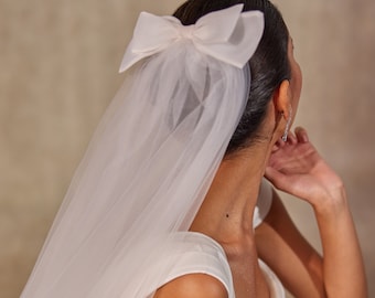 May include: A white bridal veil with a large white satin bow. The veil is made of soft tulle and is perfect for a wedding.