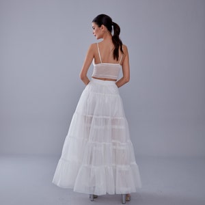 May include: A white layered tulle skirt with a white crochet top. The skirt has a high waist and is floor-length.