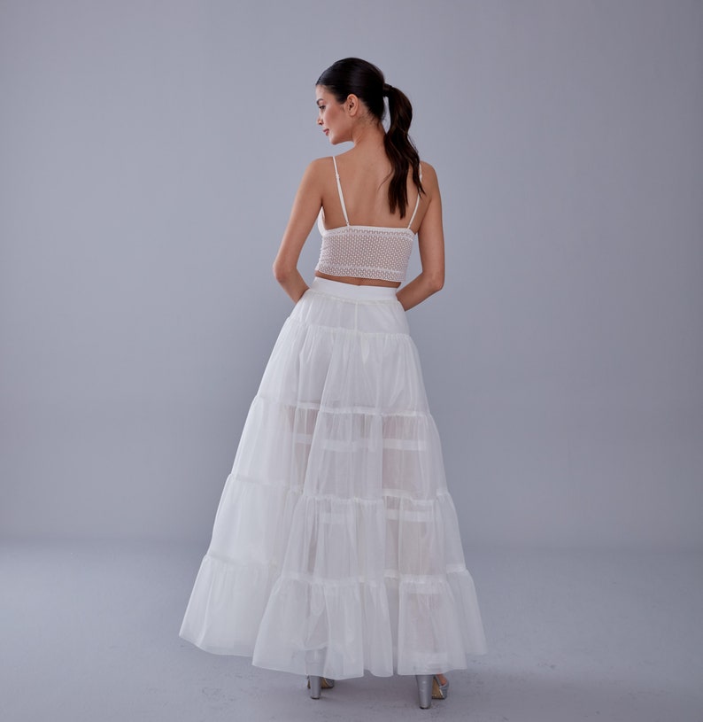 May include: A white layered tulle skirt with a white crochet top. The skirt has a high waist and is floor-length.