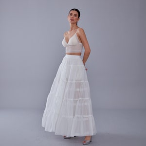 May include: A white lace crop top with a sweetheart neckline paired with a white tulle maxi skirt with multiple layers. The skirt has a flowy, romantic look.