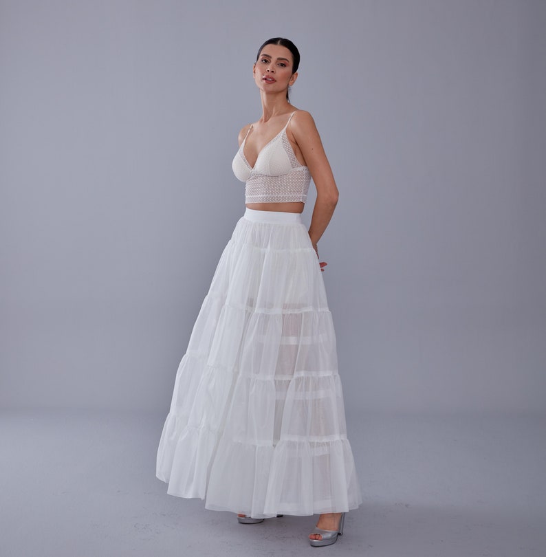 May include: A white lace crop top with a sweetheart neckline paired with a white tulle maxi skirt with multiple layers. The skirt has a flowy, romantic look.