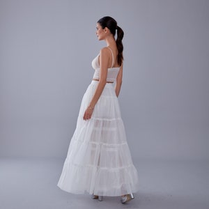 May include: A white, tiered maxi skirt with a delicate lace top. The skirt is made of a sheer fabric and has a flowy silhouette.