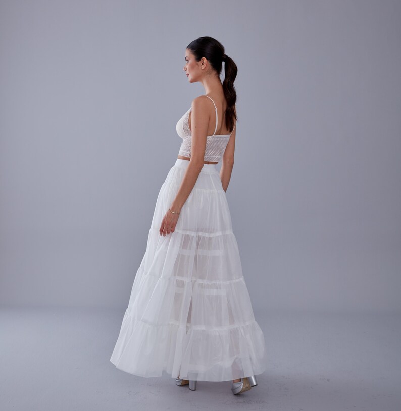 May include: A white, tiered maxi skirt with a delicate lace top. The skirt is made of a sheer fabric and has a flowy silhouette.