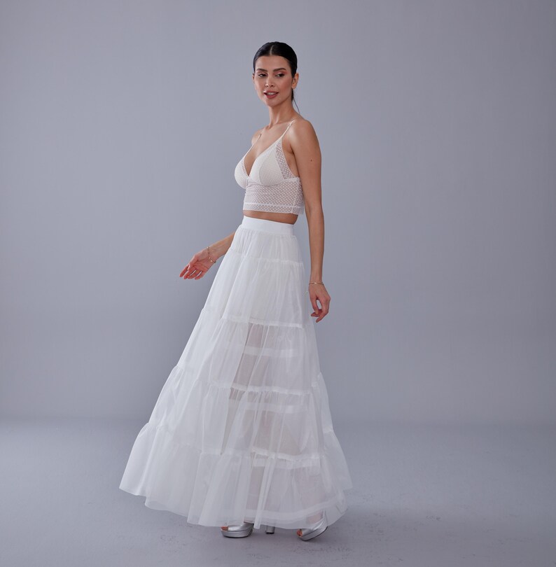 May include: A white lace crop top with a white layered tulle skirt. The model is wearing the outfit and standing on a gray background.