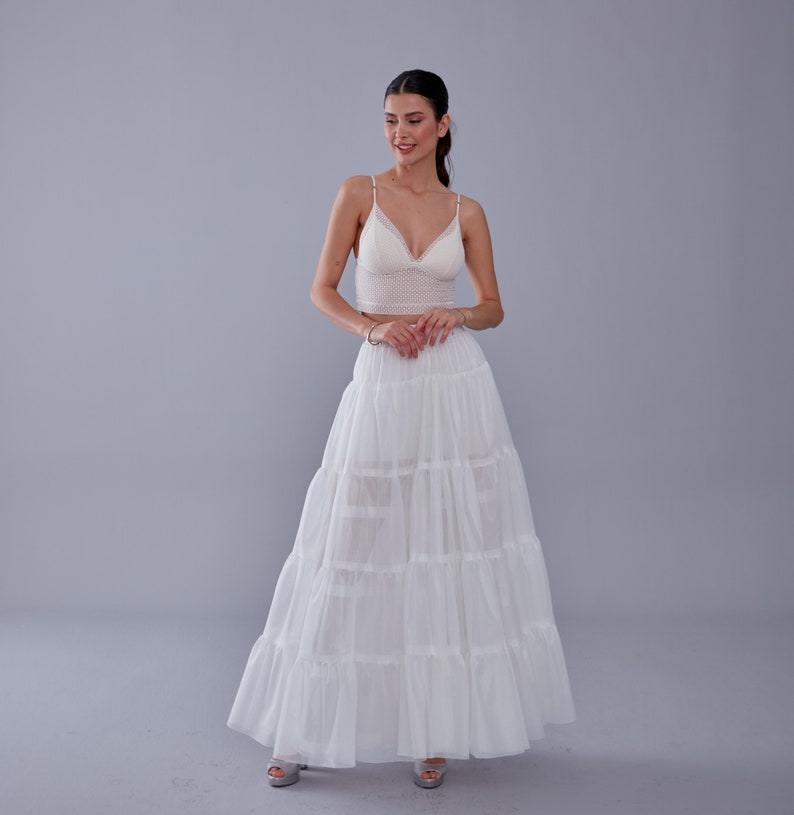 May include: A white layered maxi skirt with a ruffled hem. The skirt is made of a lightweight, flowy fabric and has a comfortable elastic waistband.