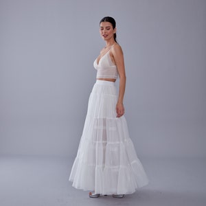 May include: A white lace crop top paired with a white tiered maxi skirt. The skirt has multiple layers of sheer fabric, creating a flowing and romantic look.