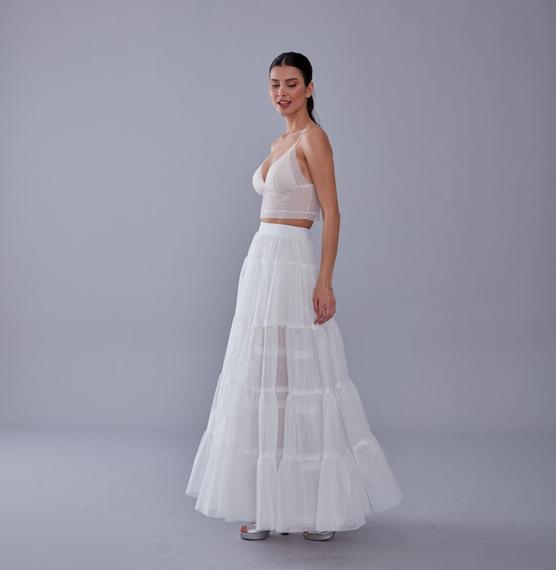May include: A white lace crop top paired with a white tiered maxi skirt. The skirt has multiple layers of sheer fabric, creating a flowing and romantic look.