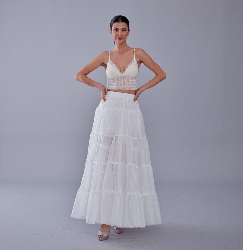 May include: A white layered tulle skirt with a white lace crop top. The model is wearing silver heels.
