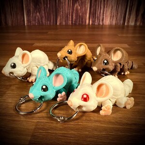 May include: Five small, colorful, plastic mouse keychains. Each mouse is in a different pose and has a different color. The keychains are attached to silver key rings.