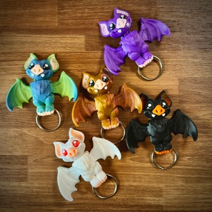 May include: Five colorful bat-shaped keychains with different colored eyes. The bats are made of a smooth, hard plastic and have a ring attached to their backs for attaching to keys.