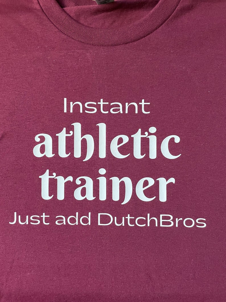 May include: Burgundy t-shirt with white text that reads "Instant athletic trainer Just add DutchBros".