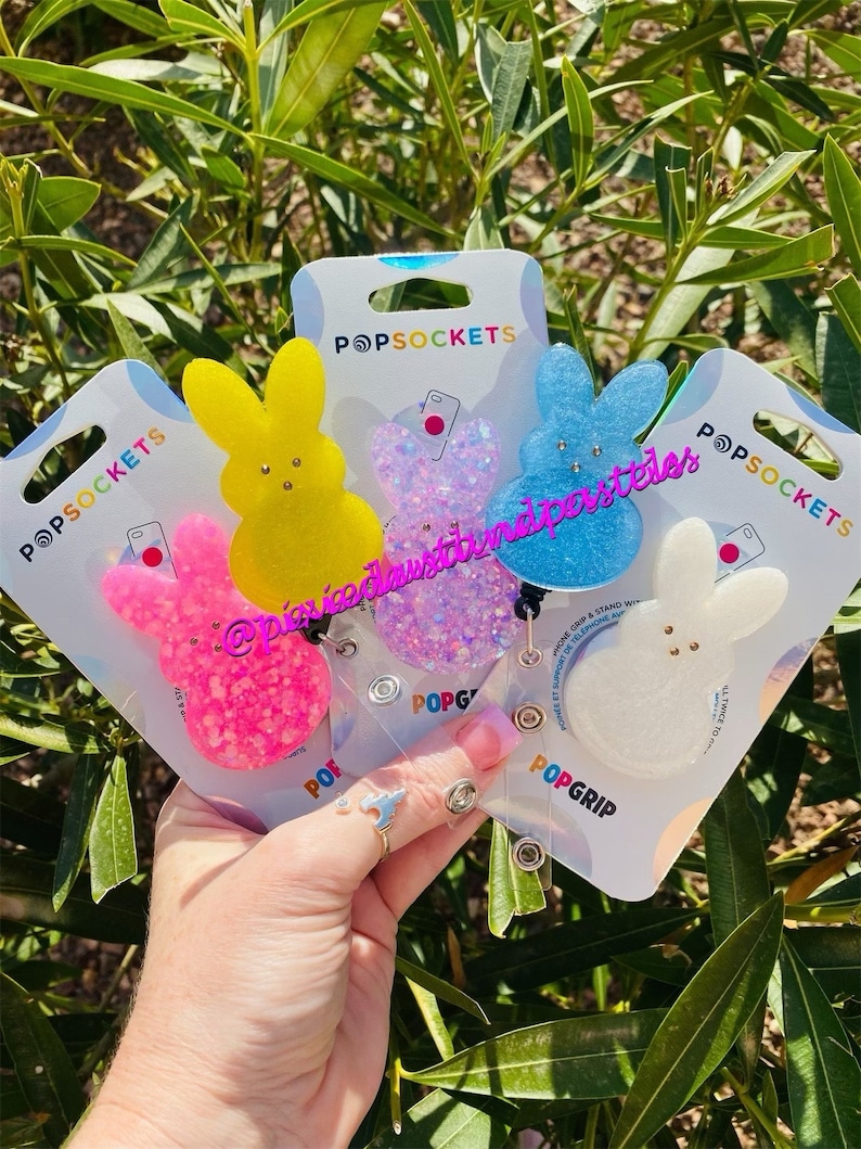 May include: Four colorful phone grips shaped like a bunny with glitter accents. The grips are attached to clear plastic cards with the text "POPSOCKETS" and "POPGRIP".