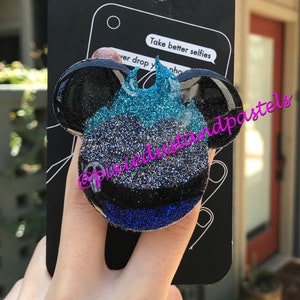 May include: A black and blue glitter PopSocket phone grip and stand with a Mickey Mouse design. The PopSocket is on a black background with the text "PopSockets phone grip & stand" and "Take better selfies".
