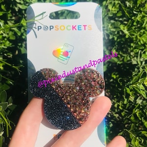 May include: A black and rose gold glitter PopSockets phone grip with a Mickey Mouse head design. The grip is on a white card with the PopSockets logo and the text "@pixiedustandpastels".