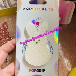 May include: White PopSocket phone grip with a bunny design. The packaging features the text "POPSOCKETS" and "POPGRIP".