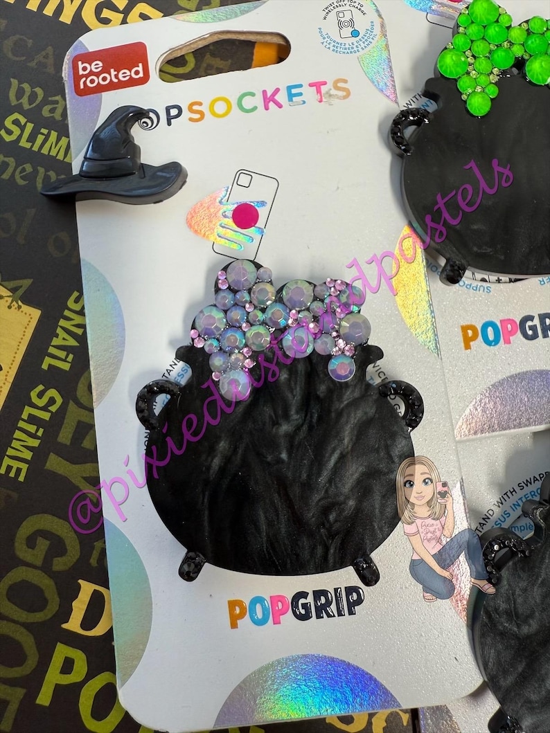 May include: Black PopSockets phone grips with a witch's hat and a cauldron design. The cauldron is embellished with iridescent rhinestones. The packaging includes the text "be rooted" and "POPGRIP".