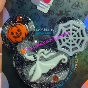 May include: A black and silver glitter phone grip with a white ghost, a pumpkin, and a spiderweb. The grip says "POPGRIP" and "APPABLE TO MESSUS ECHA".