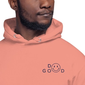 Puede incluir: Una sudadera con capucha de color rosa coral con un gráfico azul marino de una cara sonriente y el texto "DO GOOD".