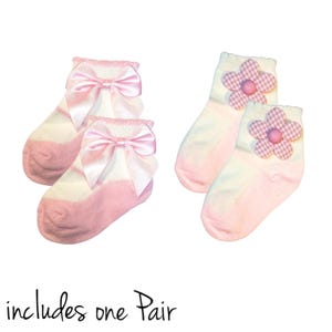 May include: Two pairs of baby socks. One pair is pink and white with a pink satin bow. The other pair is pink and white with a pink gingham flower.