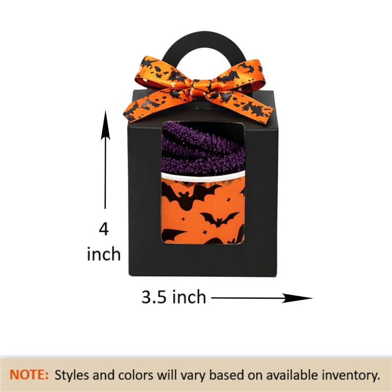 May include: A black gift box with a handle, measuring 4 inches tall and 3.5 inches wide. The box has a window revealing purple and orange Halloween-themed contents. An orange ribbon with black bat silhouettes adorns the top.