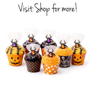 May include: Seven Halloween-themed cupcakes with various designs. The cupcakes have orange, black, and yellow frosting, and are decorated with spider toppers and decorative cupcake wrappers. The text "Visit Shop for more!" is at the top.