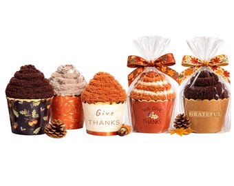 May include: Five decorative cupcake-shaped towels in various colors, including brown, tan, and orange. Some are wrapped in cellophane with decorative ribbons. The cupcakes have the words "Give Thanks" and "Grateful" printed on them. Fall-themed gift.