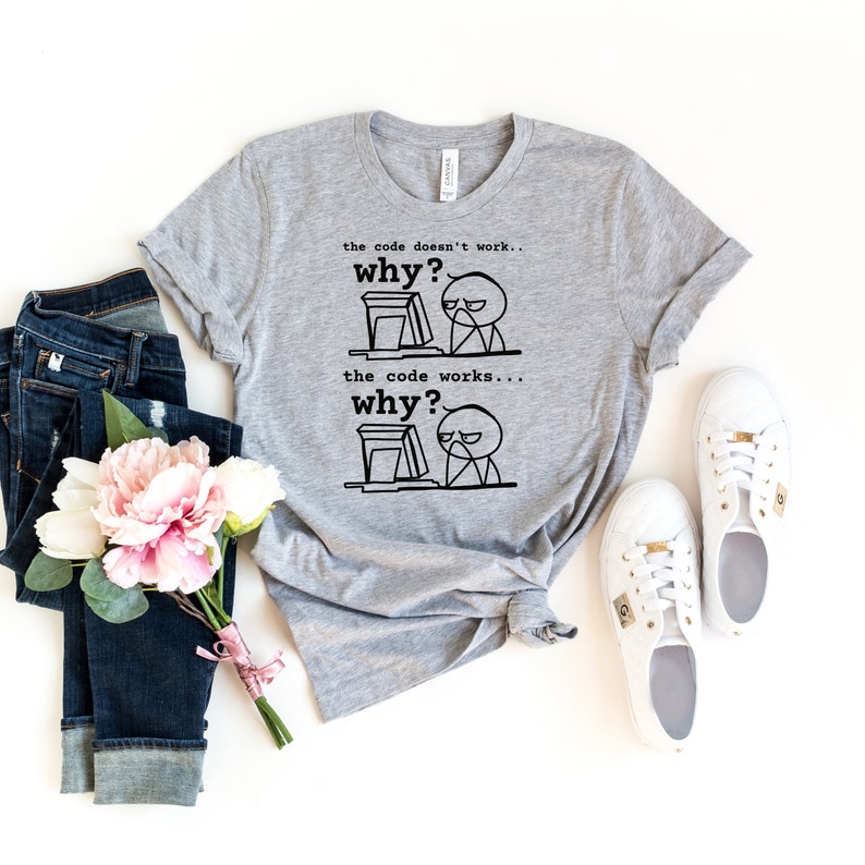Puede incluir: Camiseta gris con una ilustraci&oacute;n en blanco y negro de una persona frente a un ordenador. El texto en la camiseta dice "the code doesn't work... why?" y "the code works... why?"