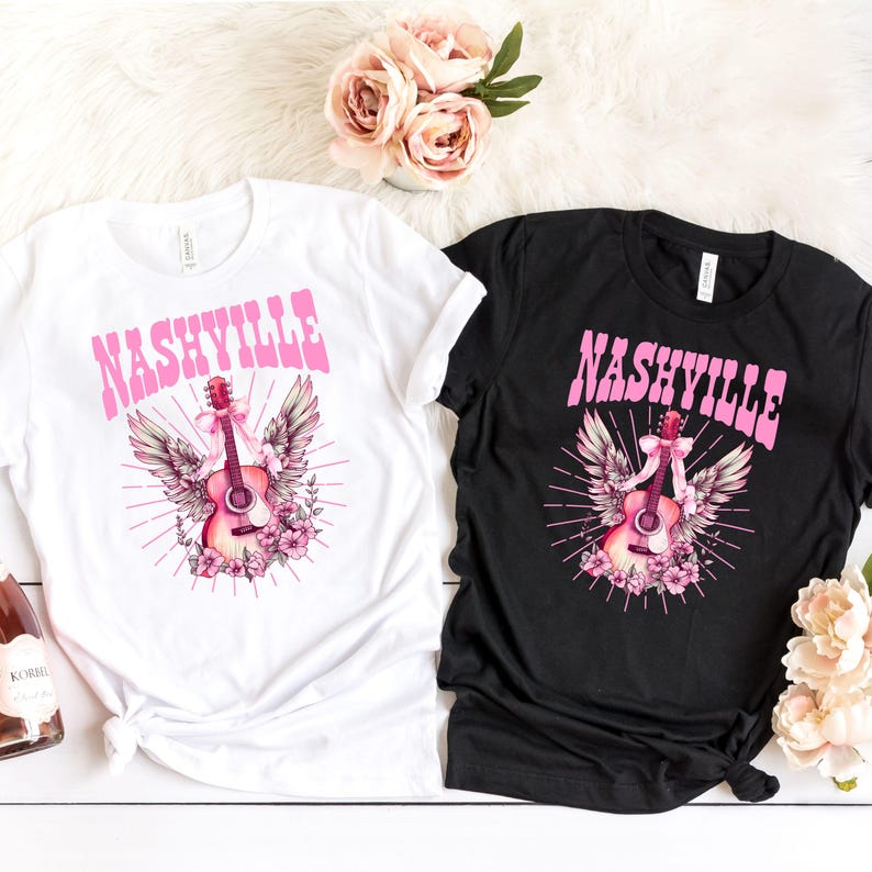 May include: Two t-shirts featuring a pink and white graphic of a guitar with wings and the word "NASHVILLE" in pink lettering. One t-shirt is white and the other is black.