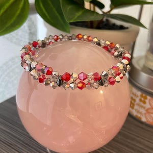 Puede incluir: Un brazalete de doble cadena hecho de cuentas de vidrio facetadas rojas y transparentes con detalles plateados.