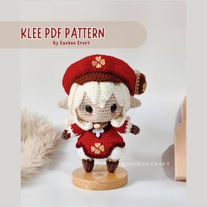 Puede incluir: Una muñeca amigurumi de crochet de Klee del videojuego Genshin Impact. La muñeca lleva un sombrero rojo con un diseño de trébol, un vestido rojo con un diseño de trébol y botas blancas. La muñeca está de pie sobre una base de madera. El texto "KLEE PDF PATTERN By Cuckoo Craft" está en la parte superior de la imagen. El texto "@Cuckoo Craft" está en la parte inferior de la imagen.