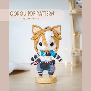 Pode incluir: Uma figura amigurumi de crochê de Gorou do videogame Genshin Impact. A figura é marrom, branca e azul com um rosto pequeno e redondo e olhos grandes e pretos. A figura está em pé sobre uma base de madeira. O texto "GOROU PDF PATTERN By Cuckoo Craft" é exibido no topo da imagem.