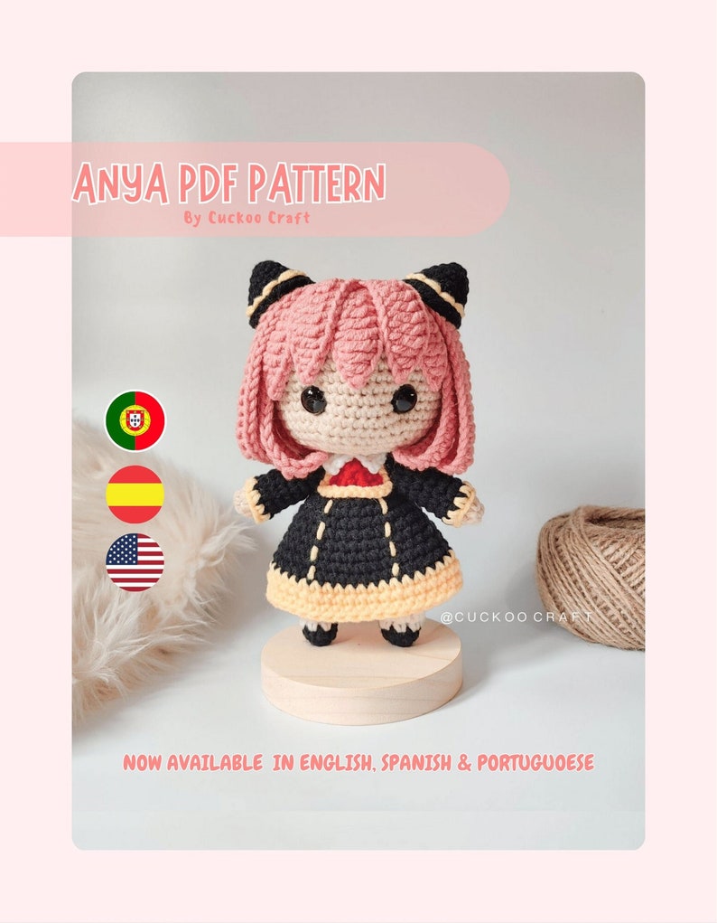 K&ouml;nnte beinhalten: Anya PDF H&auml;kelmuster, eine geh&auml;kelte Amigurumi-Puppe mit rosa Haaren, schwarzen und gelben Kleidern und Katzenohren. Die Puppe steht auf einem Holzsockel. Das Bild enth&auml;lt den Text "Anya PDF Pattern" und "By Cuckoo Craft".