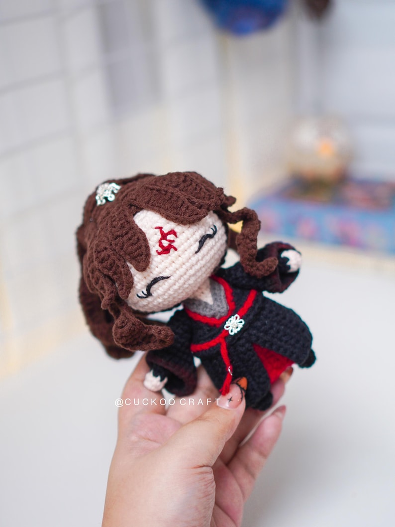 Op de afbeelding: Handgemaakte gehaakte pop met bruin haar en een zwart-rode outfit. De pop heeft een cr&egrave;mekleurig gezicht met geborduurde kenmerken en een decoratieve haarversiering. Een uniek, handgemaakt item.