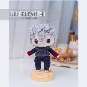 May include: Crochet amigurumi pattern for a gray haired character with a red and black outfit. The pattern is called "Till PDF Pattern" by Cucko Craft.