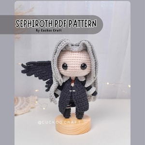 May include: A crocheted Sephiroth doll with grey hair, a black coat, and a single black wing. The doll is displayed on a wooden stand. The text "SEPHIROTH PDF PATTERN" is at the top of the image, with "By Cuckoo Craft" below it.