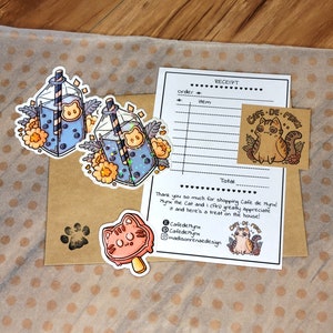 May include: A set of stickers featuring a cartoon cat with a boba tea drink. The stickers are on a brown paper background with a receipt from "Cafe de Mynx" and the text "Thank you so much for shopping Cafe de Mynx Mynx the Cat and I (Ari) greatly appreciate it and here's a treat on the house!"  The receipt also includes the text "Cafede Mynx" and "madisonrenaedesign".