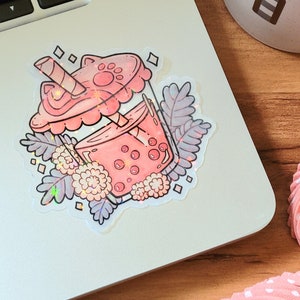 K&ouml;nnte beinhalten: Ein rosa-wei&szlig;er Aufkleber mit einem Boba-Tee-Becher mit einem Pfotenabdruck auf dem Deckel, umgeben von Blumen und Bl&auml;ttern.