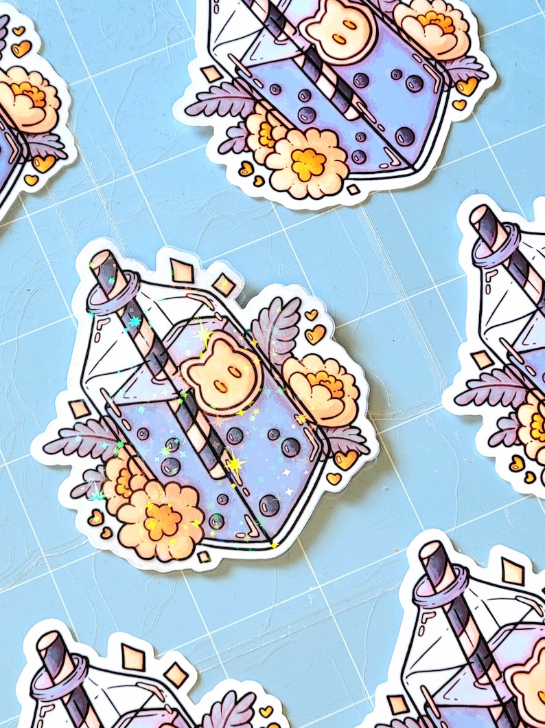 May include: A sticker featuring a cartoon illustration of a glass bottle filled with a blue drink with boba pearls and a straw. The bottle is decorated with flowers and hearts. The sticker is printed on white paper.